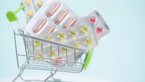 close up view of small shopping cart with pills on blue background   - 写真・画像