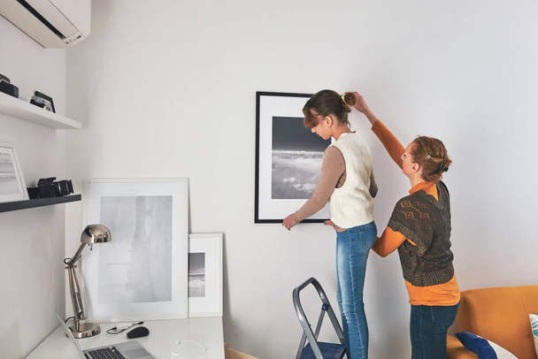 Mother and daughter hanging pictures and photos at home. - Photo, Image