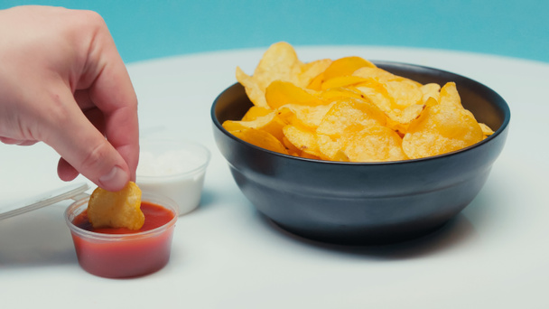 vista parziale dell'uomo immergendo patatine increspate in ketchup su blu - Foto, immagini