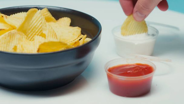 ridged potato chips in bowl near containers with ketchup and mayonnaise on blue - Foto, Imagem