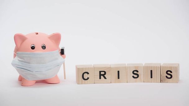 piggy bank in protective medical mask and cubes with crisis word on white surface - Foto, Bild