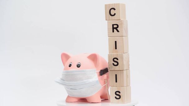 piggy bank in medical mask and blocks with crisis word on white surface - Zdjęcie, obraz