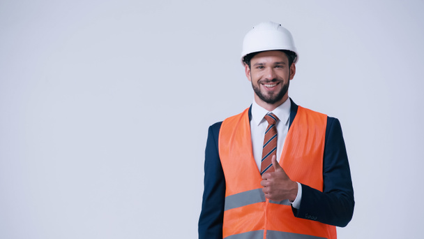 happy foreman in safety vest and helmet showing thumb up isolated on grey - Фото, изображение
