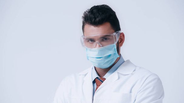brunetka vědec v lékařské masce a brýle při pohledu na kameru izolované na šedé - Fotografie, Obrázek