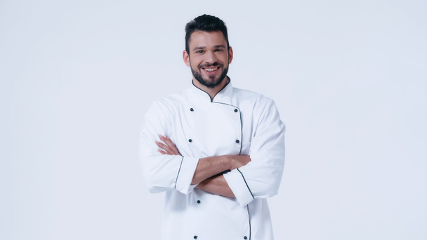 молодой и счастливый человек в пиджаке шеф-повара, стоящий со скрещенными руками изолированный на белом - Фото, изображение