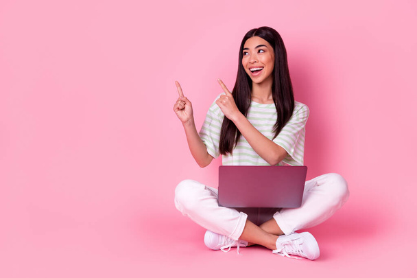 Full size photo of pretty positive vietnamese girl sit floor look indicate fingers empty space isolated on pink color background. - Fotoğraf, Görsel