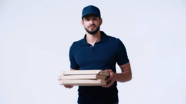 young delivery man in blue uniform holding pizza boxes and looking at camera isolated on white - Foto, afbeelding
