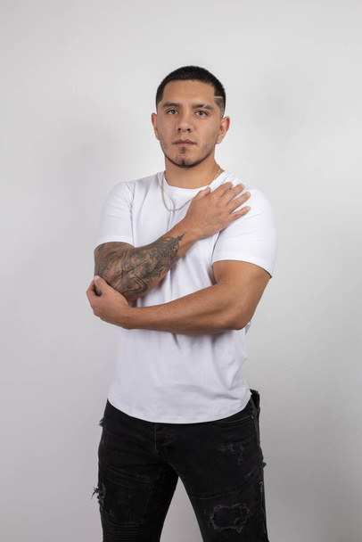 umarmt sich lateinischer junger Mann mit kurzen urbanen Frisuren trägt weißes T-Shirt, Studio grundlegende Mode und gesunden Lebensstil, Wellness - Foto, Bild