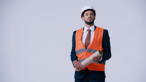 serious architect in formal wear and safety vest holding blueprint tube isolated on grey - Фото, зображення