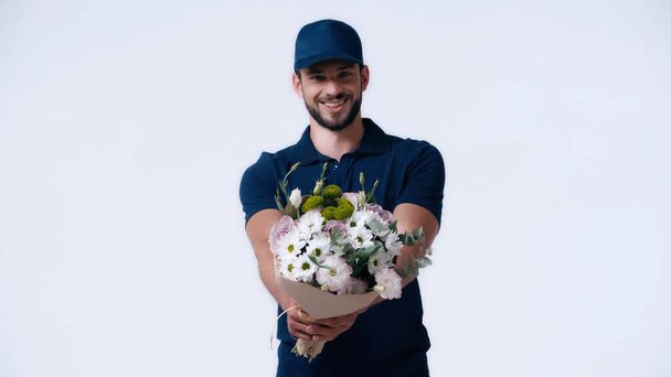 szczęśliwy dostawca człowiek w niebieskim mundurze gospodarstwa kwiaty izolowane na białym - Zdjęcie, obraz
