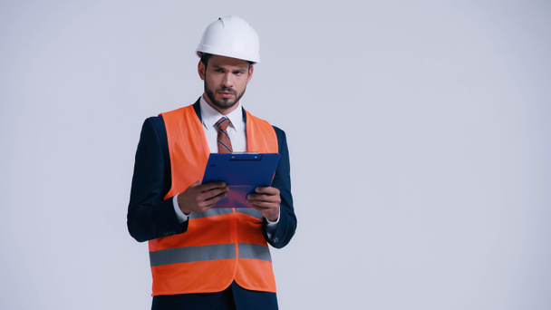 serious contractor in hardhat holding clipboard and looking away isolated on grey - Foto, Bild