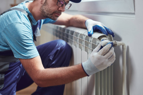 Centrale verwarming monteur en klusjesman repareren van huis radiator, gas crisis en seizoensgebonden kwesties. - Foto, afbeelding