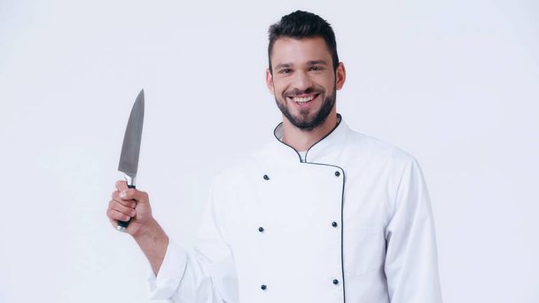vrolijk chef in uniform met scherp mes en kijkend naar camera geïsoleerd op wit - Foto, afbeelding