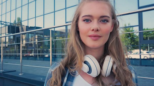 Portrait of blonde woman with headphones looking at camera on urban street  - Zdjęcie, obraz