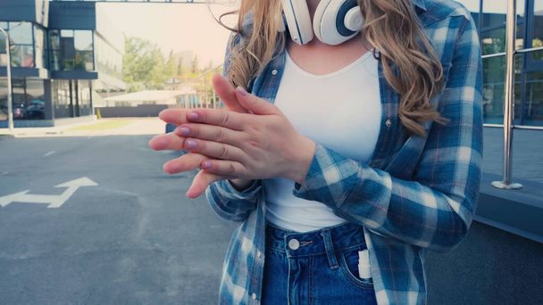 Καλλιεργημένη άποψη της γυναίκας με ακουστικά ξήρανση απολυμαντικό στα χέρια σε εξωτερικούς χώρους  - Φωτογραφία, εικόνα