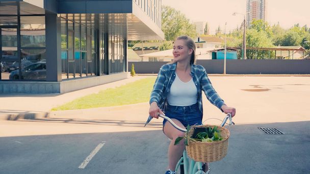 Улыбающаяся блондинка на велосипеде по городской улице  - Фото, изображение