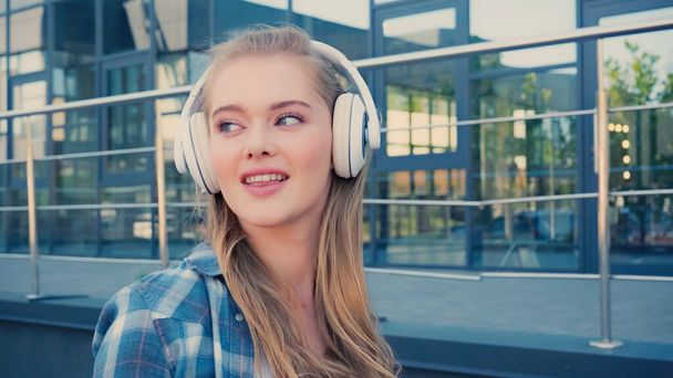 Positive woman listening music in headphones on urban street  - Zdjęcie, obraz