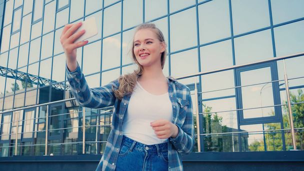 Blonde woman taking selfie on smartphone on urban street  - Foto, Imagem