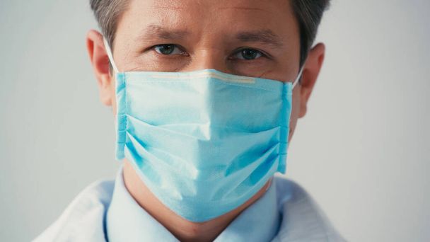 portrait of doctor in medical mask looking at camera isolated on grey - 写真・画像