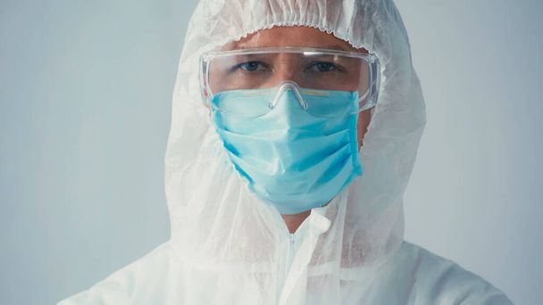 Porträt eines Wissenschaftlers in Schutzanzug und Schutzbrille mit medizinischer Maske, der isoliert auf graue Kamera blickt - Foto, Bild
