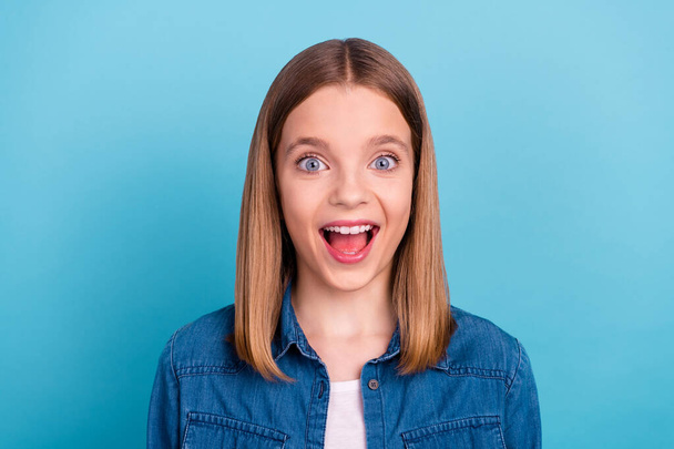 Photo of impressed small blond girl look empty space wear jeans shirt isolated on blue color background. - Foto, afbeelding