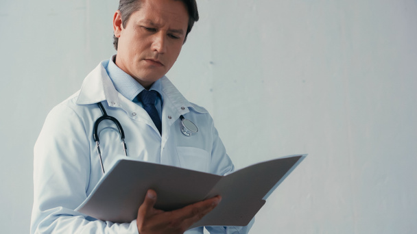 Beyaz önlüklü düşünceli doktor gri arkaplandaki dosyaları okuyor. - Fotoğraf, Görsel