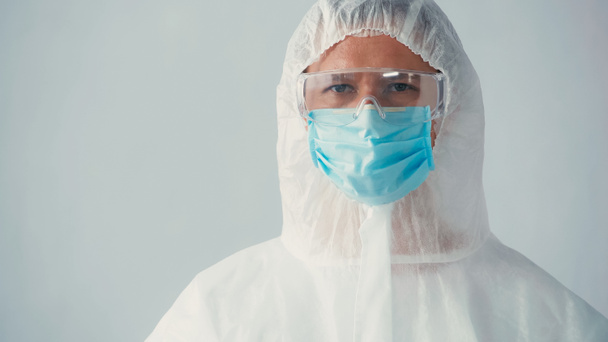 ピンクのスーツを着た免疫学者の肖像とグレーで隔絶されたカメラを見る医療用マスクを持つゴーグル - 写真・画像
