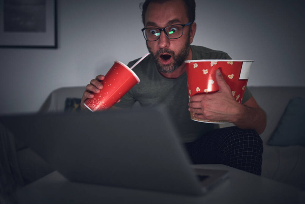 Hombre adulto viendo películas en casa, comiendo palomitas de maíz y bebiendo jugo. - Foto, imagen