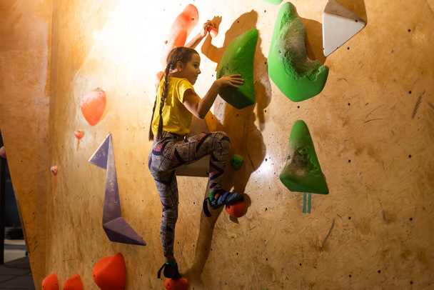 bouldering, niña trepando por la pared y escalador agarres multicolores. Actividades de ocio. - Foto, imagen