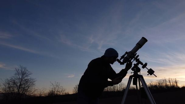 Σιλουέτα ενός άνδρα, τηλεσκόπιο και εξοχή κάτω από τον ουρανό το βράδυ. - Φωτογραφία, εικόνα