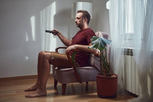 Homme adulte regardant la télévision à la maison et tenant une télécommande. - Photo, image