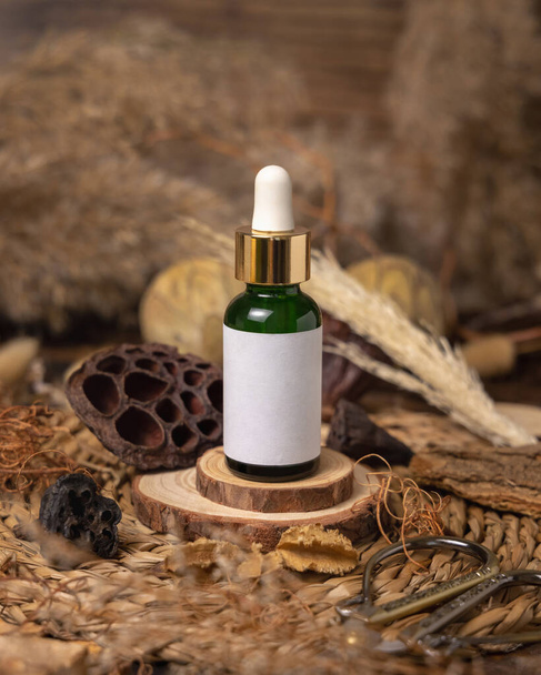 Green glass dropper bottle on wood near natural boho decorations close up, cosmetics label mockup. Eco friendly Skincare beauty product, serum or essence. Bohemian composition with dried leaves and flower - Photo, Image
