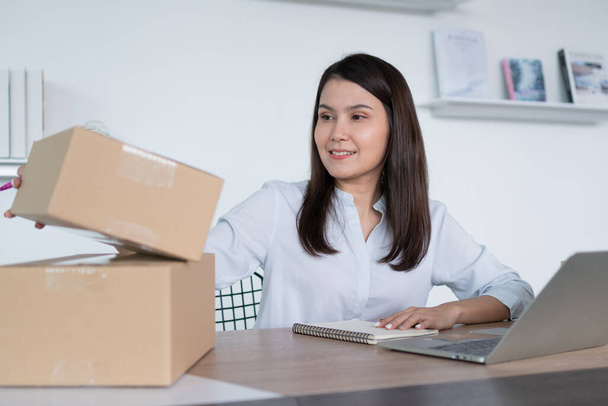 Happy young Asian woman entrepreneur, Hold package and Smile for sale success of online shopping store at home office, Concept of merchant, small business, online business and eCommerce. - Фото, зображення