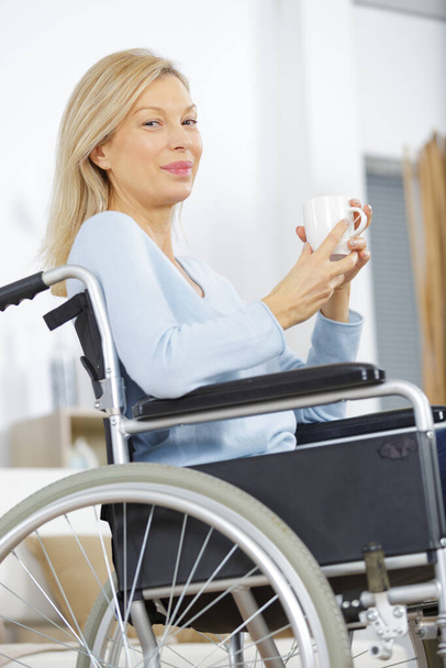 disabled woman in wheelchair at home reading newspaper and drink - Foto, Bild