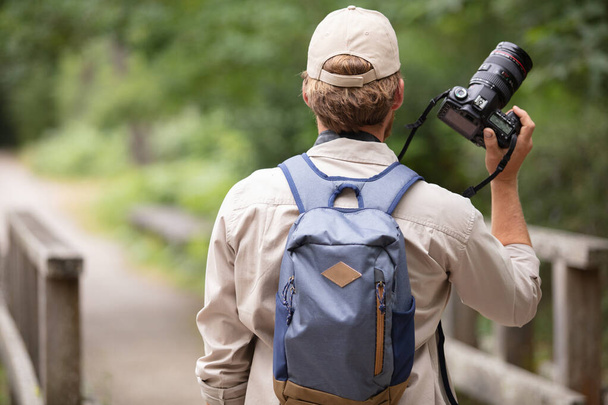 rear view of man wearing rucksack and holding camera - Photo, Image
