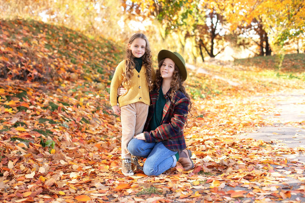 Mladá krásná šťastná dvě malé holčičky v podzimním oblečení. Šťastné sestřičky objímající se na podzimním pozadí na Halloween. Usmívající se přítelkyně procházející se v podzimním parku. koncept šťastná rodina, dětství - Fotografie, Obrázek