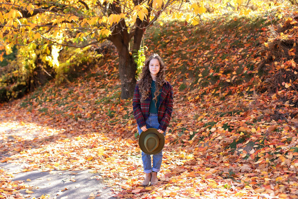 Glückliches junges Mädchen mit Hut und Herbstkleidung auf herbstlichem Hintergrund. Ein lächelndes Mädchen spielt im Herbstpark. Junges Mädchen hat Spaß beim Spielen mit fallenden goldenen Blättern. Herbst Porträt von niedlichen Mädchen - Foto, Bild