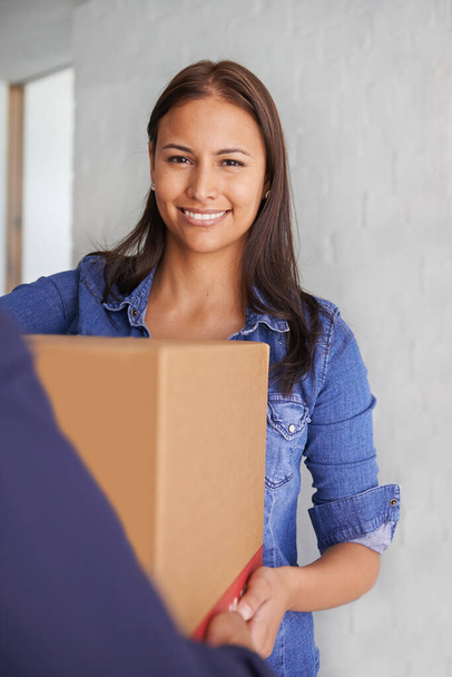 Eine schöne junge Frau lächelt in die Kamera, als sie eine Schachtel von einem Umzugsunternehmen entgegennimmt - Foto, Bild