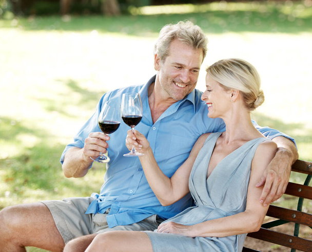 Destressing together. Happy mature couple toasting their love with two glasses of wine while outdoors - Photo, Image