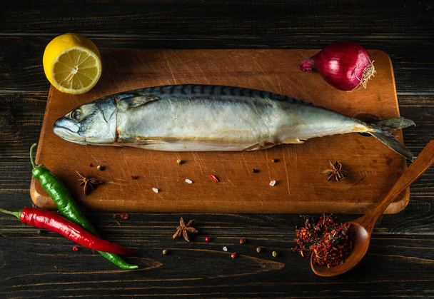 Mutfak masasında çiğ uskumru balığı, balık yemi pişirmeden önce malzeme ve baharatla tahta kesiyor. Reklam için boş alan. - Fotoğraf, Görsel