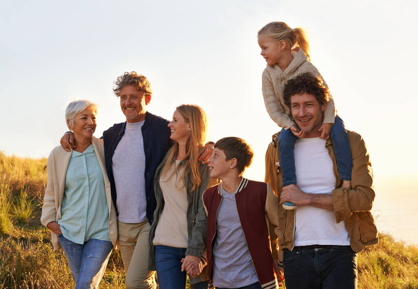 Vyhlídková večerní procházka s těmi, které milují nejvíc. šťastná multigenerační rodina kráčející po travnatém kopci mraveniště západ slunce - Fotografie, Obrázek
