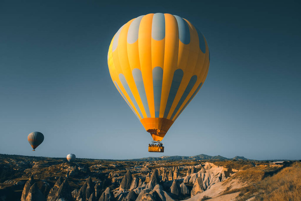 Yellow bright hot air balloon with tourists rise up for sunrise watching. Wide blue sky landscape of Goreme valley in Cappadocia. Tourism, travel, holidays, recreation background, concept postcard - Photo, Image