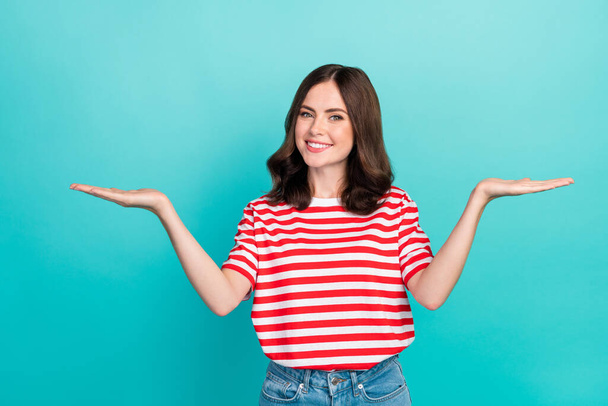 Photo of young cute nice pretty gorgeous woman wear red striped t-shirt hold palms compare products difference smile isolated on cyan color background. - Fotó, kép