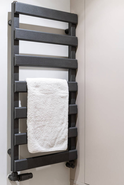 Boční pohled na čisté čisté čisté koupel ručník visí na černé elektrické sušičky racku. Topný radiátor instalovaný na stěně v koupelně. Koncepce spotřebního a energeticky účinného spotřebiče pro domácnost - Fotografie, Obrázek