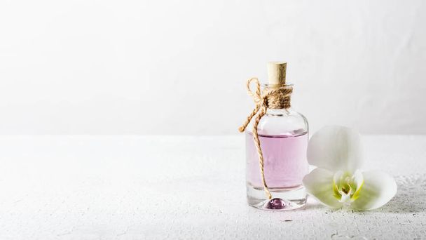 Rose esenciální olej ve skleněné láhvi a orchidej květiny na bílém pozadí. - Fotografie, Obrázek