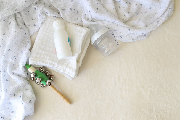 Newborn baby care items are on the table. A muslin swaddle, a cute rattle, powder and a baby bottle with a pacifier. Place for text. Nobody. Top view. - Φωτογραφία, εικόνα