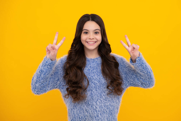 Happy teenager, positive and smiling emotions of teen girl. Teenager child girl showing fingers victory sign. Number two, v-sign symbol isolated on yellow background - Foto, afbeelding