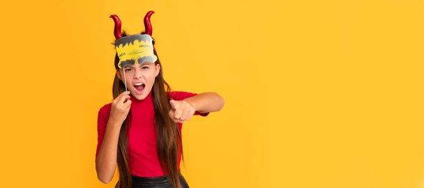 devil kid with pumpkin. trick or treat. teen girl point finger on yellow background. Halloween kid girl portrait, horizontal poster. Banner header with copy space - Foto, Imagem