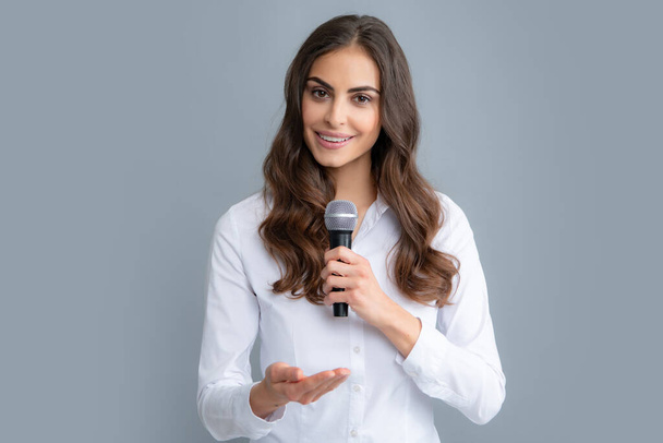 Nyilvános beszéd mikrofonnal, beszédbemutató koncepció. Gyönyörű elegáns nő énekel karaoke elszigetelt szürke háttér - Fotó, kép