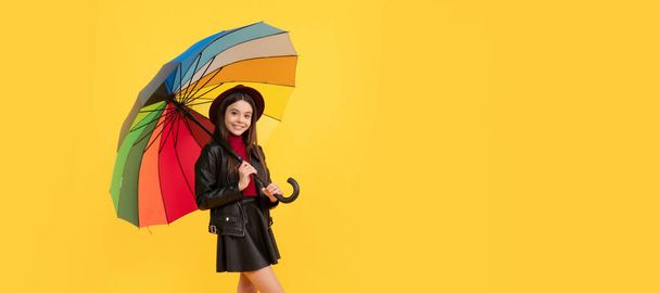 happy teen girl in hat and leather clothes under rainbow umbrella, autumn weather. Child with autumn umbrella, rainy weather, horizontal poster, banner with copy space - Foto, imagen